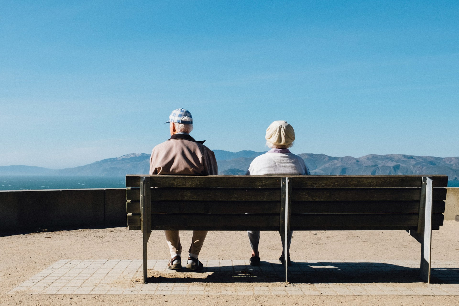 Zwei ältere Menschen sitzen auf einer Bank und blicken aufs Meer